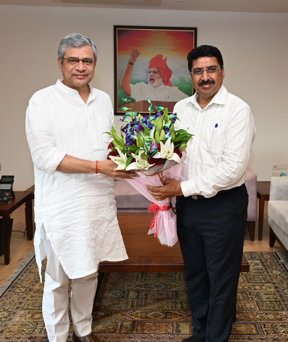 Deepak Mhaskey standing with a Union Minister during an official call, exchanging a bouquet of flowers in a formally furnished office.