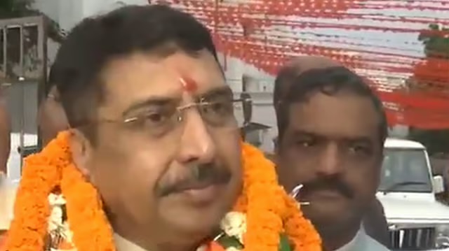Deepak Mhaskey wearing marigold garlands outdoors, with supporters and decorated vehicles visible behind him.