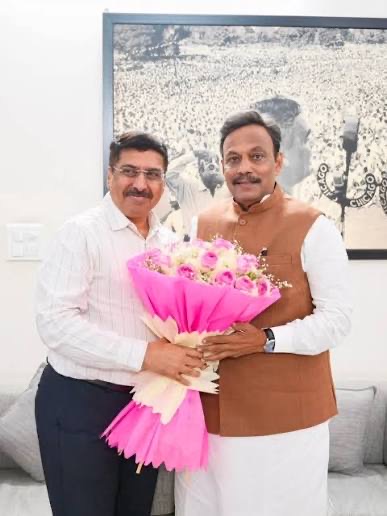 Deepak Mhaskey, wearing a saffron scarf over a white kurta, standing with a senior party leader in a hall, presenting a bouquet of flowers.